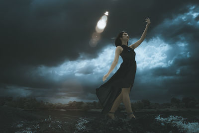 Young woman standing against cloudy sky