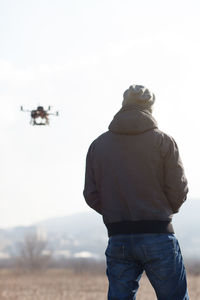 Rear view of mid adult man flying drone against clear sky