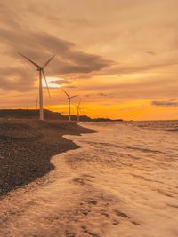 Windmills by sea against sky during sunset