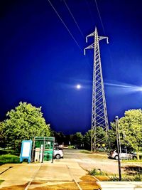 Electricity pylon by road against sky at night