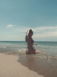 Rear view of woman standing at beach against sky