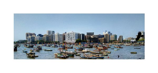 Boats moored in city by buildings against clear sky