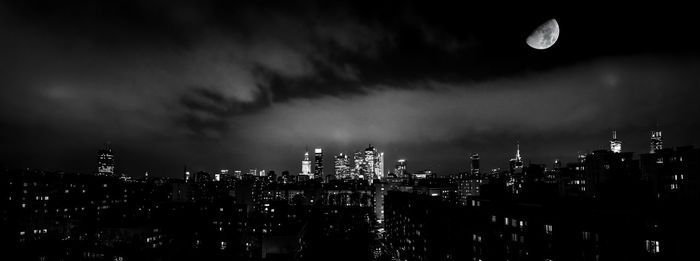 Illuminated modern buildings in city against sky at night