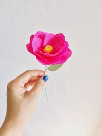 Close-up of human hand holding artificial pink flower against wall