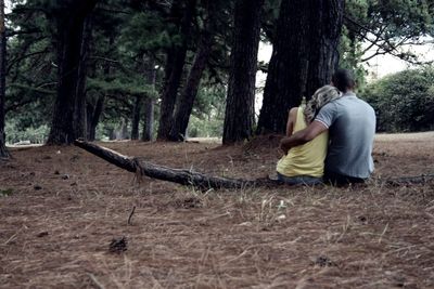 Rear view of couple sitting on fallen branch at field