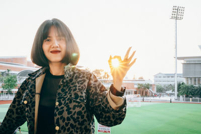 Portrait of woman showing ok sign while standing in stadium against sky