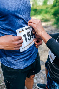 Midsection of man attaching marathon bib while standing in forest