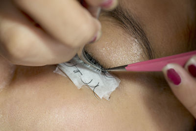 Cropped hands of beautician applying false eyelashes to woman