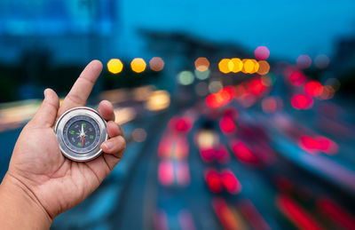 Close-up of hand holding navigational compass against illuminated lights