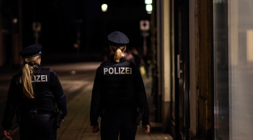 Rear view of policewomen walking on sidewalk in city at night