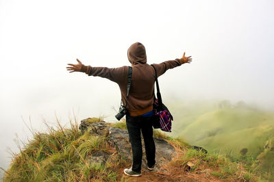 Rear view of woman with arms raised standing against sky