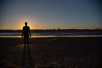 Silhouette man standing on beach against sky during sunset