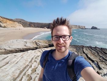 Portrait of man smiling while standing on rocky shore at beach