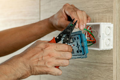 Stripping electrical wires in a plastic box on a wooden wall to install the electrical outlet.