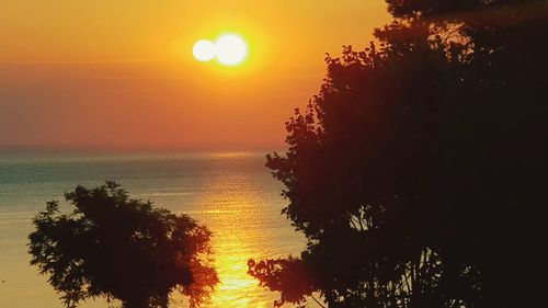 Silhouette tree by sea against orange sky