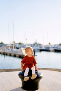 Boy sitting on pier against sky