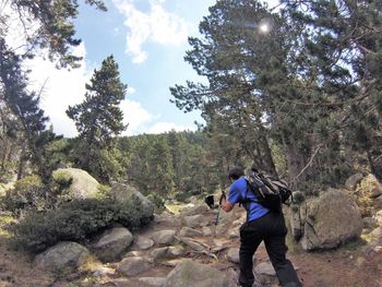 Rear view of man climbing amidst trees in forest against sky