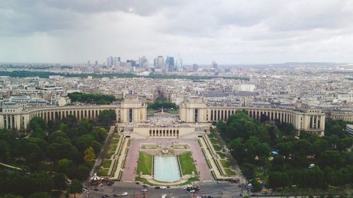 High angle view of trocadero gardens in front of cityscape against cloudy sky