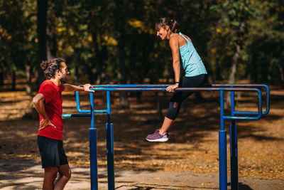 Woman exercising on parallel bar in the park with personal trainer