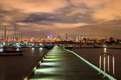 Illuminated pier amidst buildings against sky at night