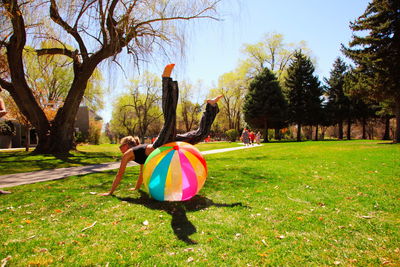 Full length of woman playing with multi colored ball in park against sky