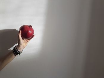 Midsection of woman with red apple against wall