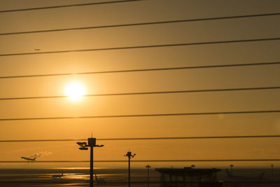 Low angle view of silhouette cables against orange sky