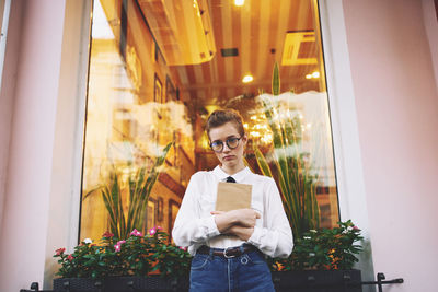 Portrait of young woman standing against window