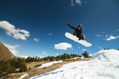 Young woman athlete doing a trick in a jump on a snowboard against a background of blue sky