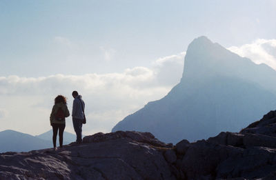 Rear view of men standing on rock against sky