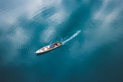 Aerial view of small powerboat floating through calm rippling turquoise lake water in sunny day