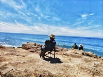 Rear view of men sitting at beach against sky