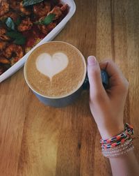 Cropped image of woman holding cappuccino at table