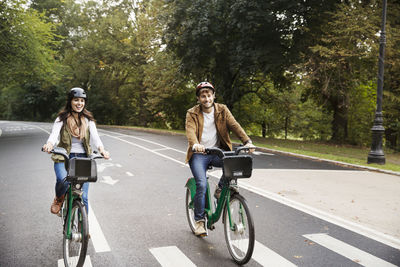 Cheerful couple riding bicycle on road at park