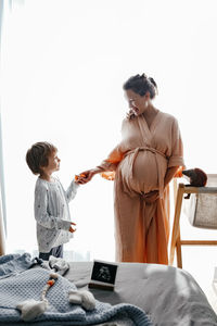 Side view of pregnant mom and her little son expecting newborn baby and preparing clothes for baby