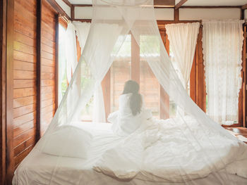 Backside of woman stretching in bed after wake up, happy greets new day with warm sunlight.