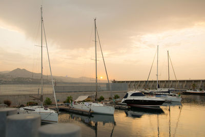 Sailboats moored in harbor at sunset