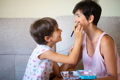 Daughter applying make-up on mother while sitting at home