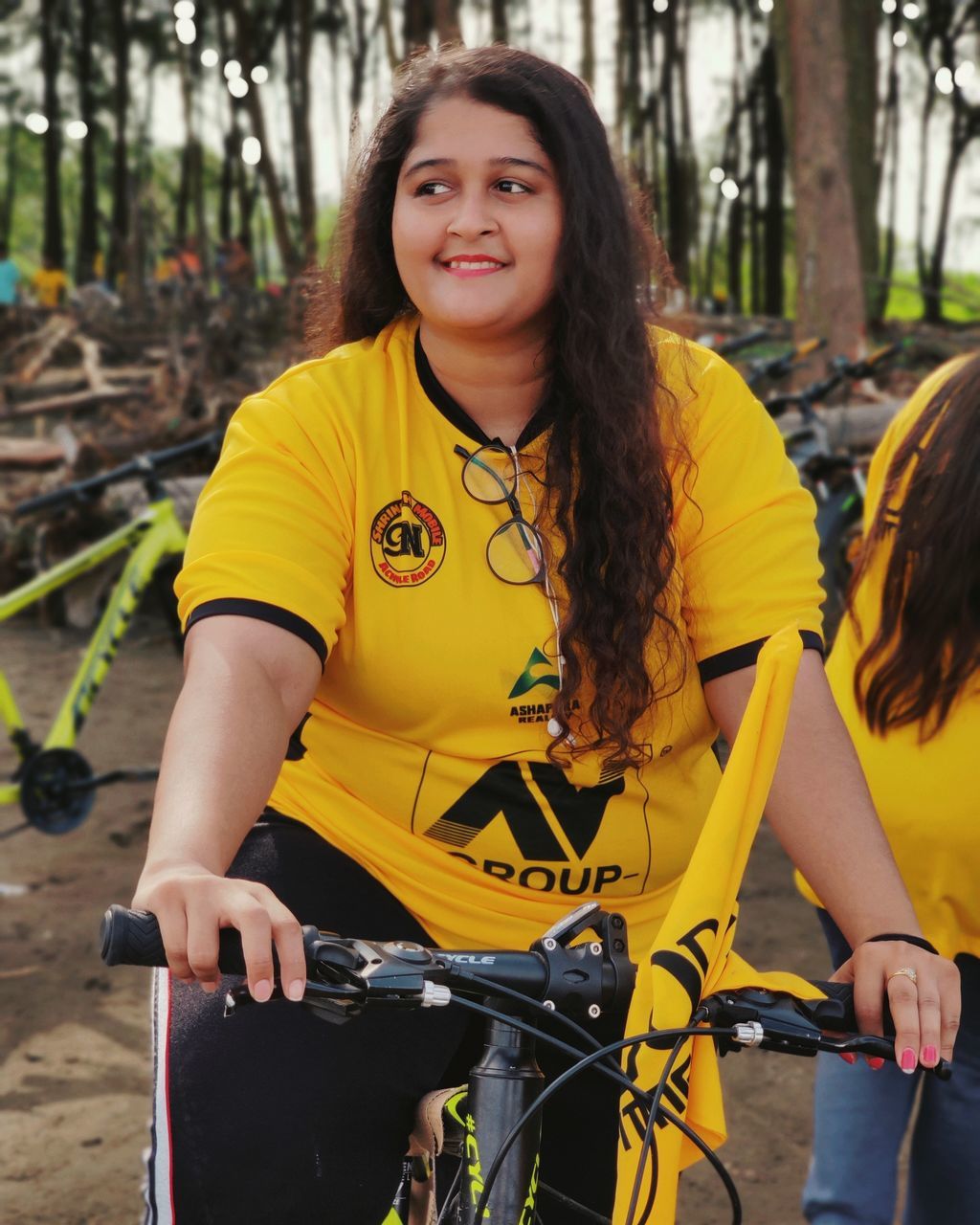 real people, lifestyles, looking at camera, yellow, leisure activity, portrait, one person, bicycle, three quarter length, hairstyle, front view, smiling, transportation, tree, casual clothing, long hair, day, nature, mode of transportation, hair, outdoors, riding