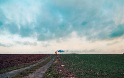 Rear view of woman holding distress flares on field against sky