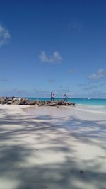 Distant view of men walking at beach against blue sky