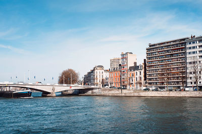 Bridge over river by buildings in city against sky