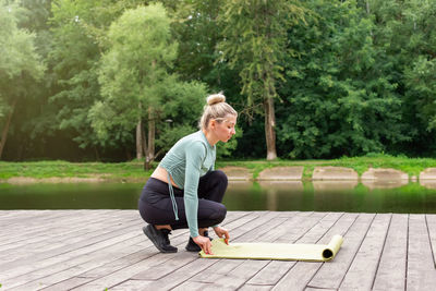 A blonde in the summer in the park, unwinds a green gym mat, prepares for sports.