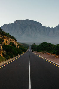 Empty road leading towards mountains against sky.