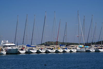 Sailboats moored in harbor against clear blue sky