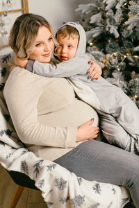 Pregnant mother with son sitting by christmas tree