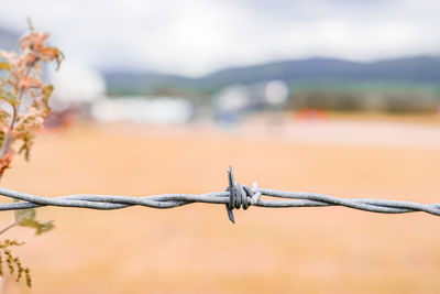 Close-up of barbed wire fence against sky