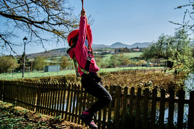 Little girl with protections practicing climbing between trees with ropes and nets