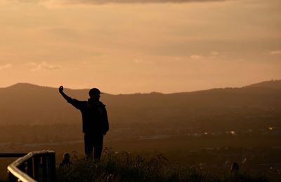 Rear view of silhouette man standing on land against sky during sunset