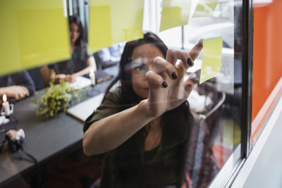 Close-up of creative businesswoman sticking adhesive note on window seen through glass